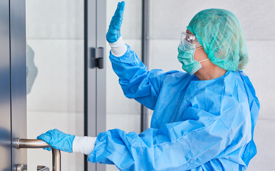 Healthcare Worker in Full PPE Waving in Front of Hospital Door