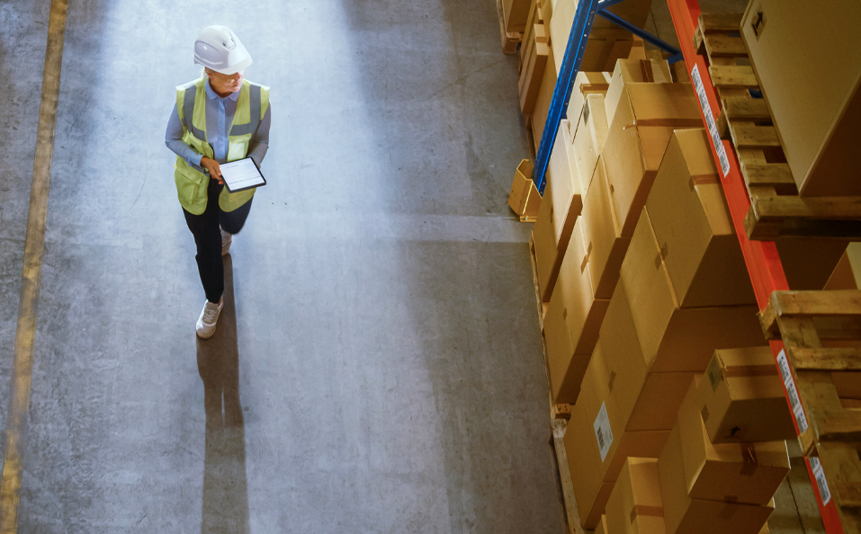 Worker with Hard Hat and Tablet Looking at Boxes in Distribution Facility